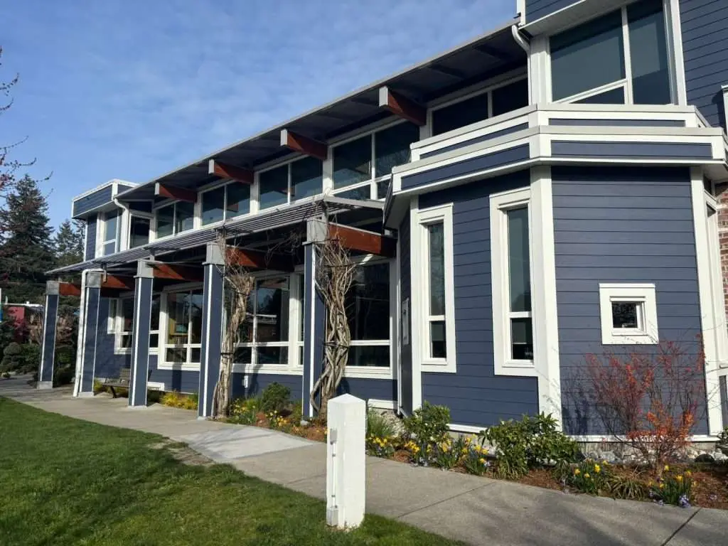 Modern blue exterior of Sechelt Municipal Hall featuring new white fiberglass window systems and prominent wood support beams under a clear sky.