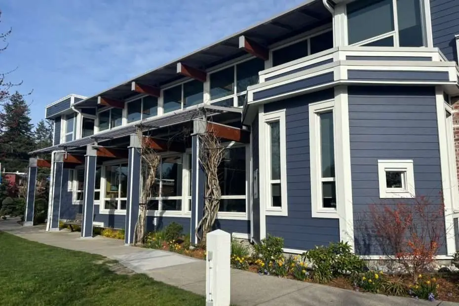 Modern blue exterior of Sechelt Municipal Hall featuring new white fiberglass window systems and prominent wood support beams under a clear sky.